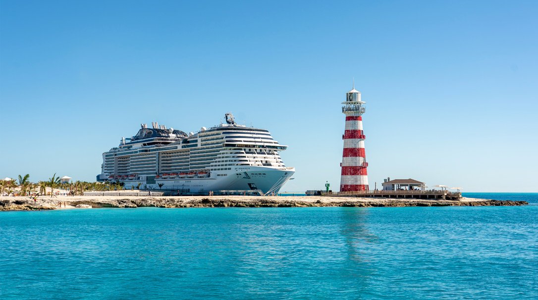 A large MSC cruise ship docked near a red and white striped lighthouse | MSC Cruises A large MSC cruise ship docked near a red and white striped lighthouse | MSC Cruises
