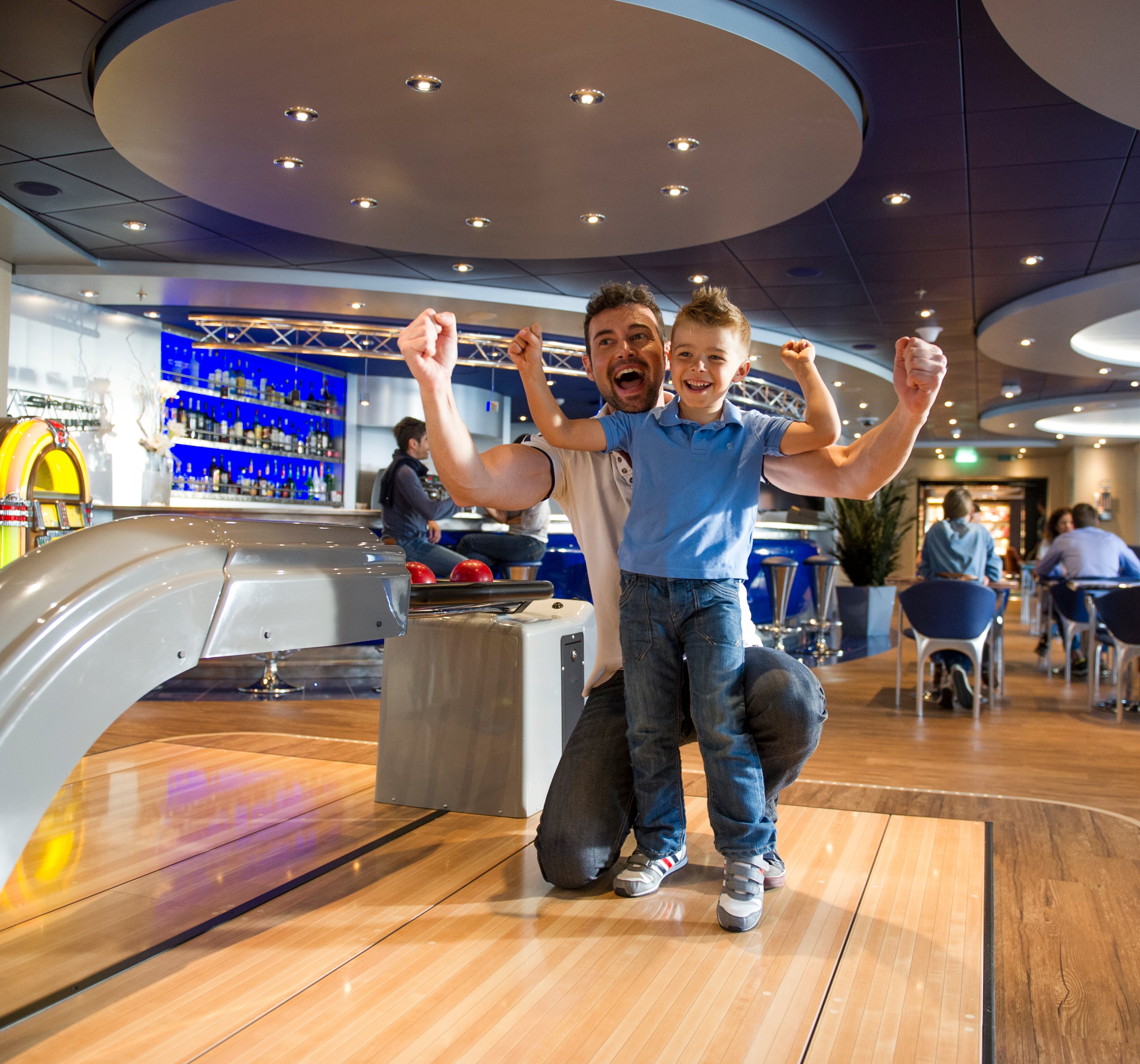 Father and son enjoying bowling onboard a cruise ship with a vibrant lounge in the background | MSC Cruises Father and son enjoying bowling onboard a cruise ship with a vibrant lounge in the background | MSC Cruises