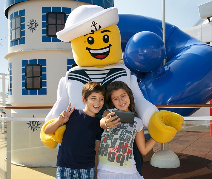 Children taking a selfie with a LEGO sailor mascot on an MSC cruise ship deck | MSC Cruises